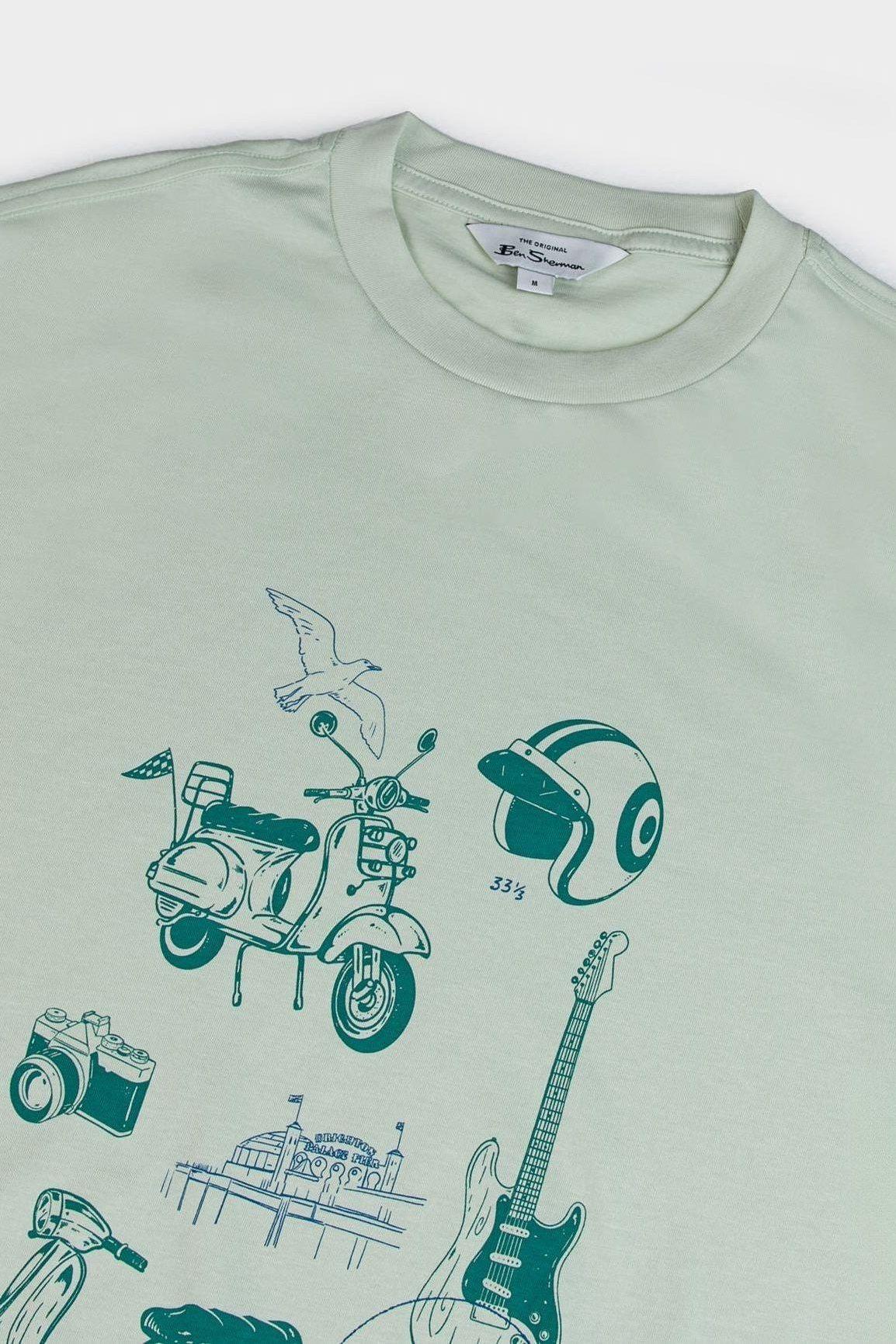 Close-up of the pistachio t-shirt’s chest graphic showing vintage-style illustrations including a scooter, helmet, guitar, and seaside pier in teal ink.